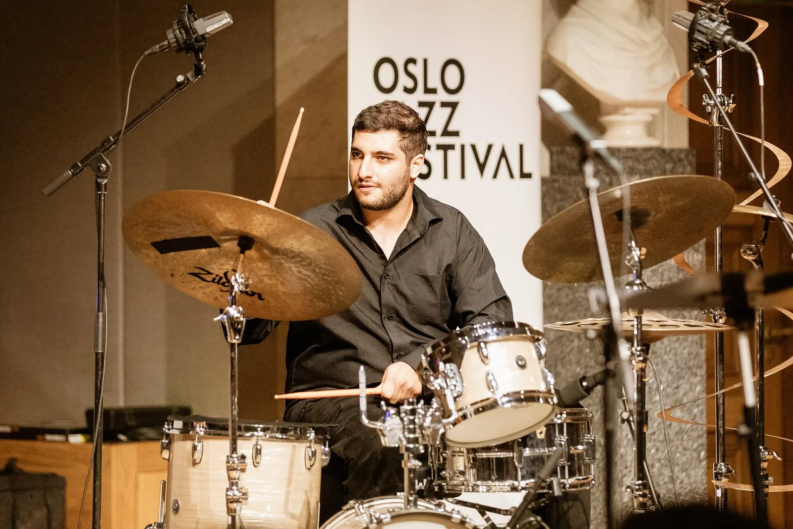 A drummer playing a kit on a festival stage, cymbals catching the light, with the Oslo Jazz Festival logo behind him.