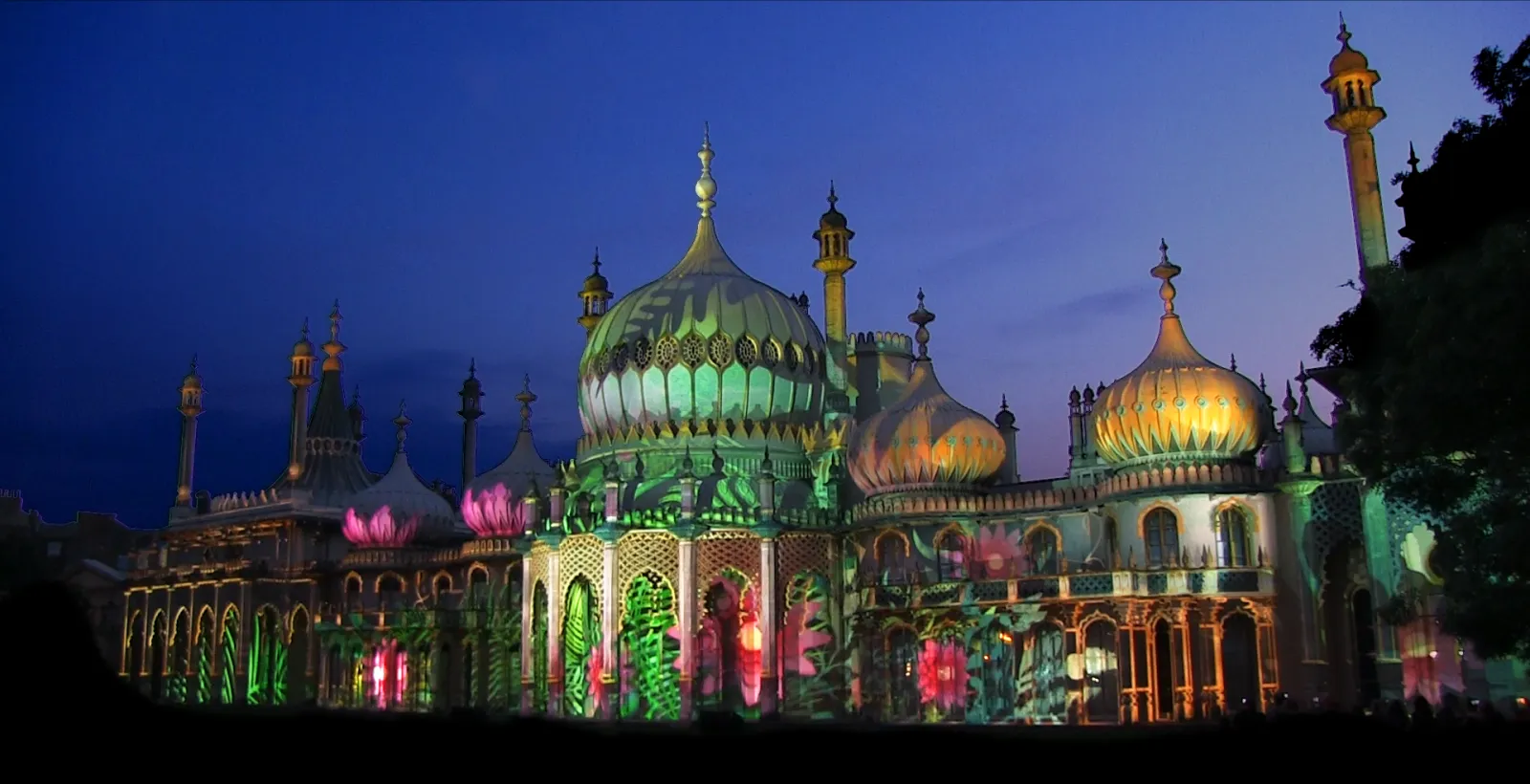 The Royal Pavilion in Brighton at night, its domes and facade covered in projected colour and patterns.