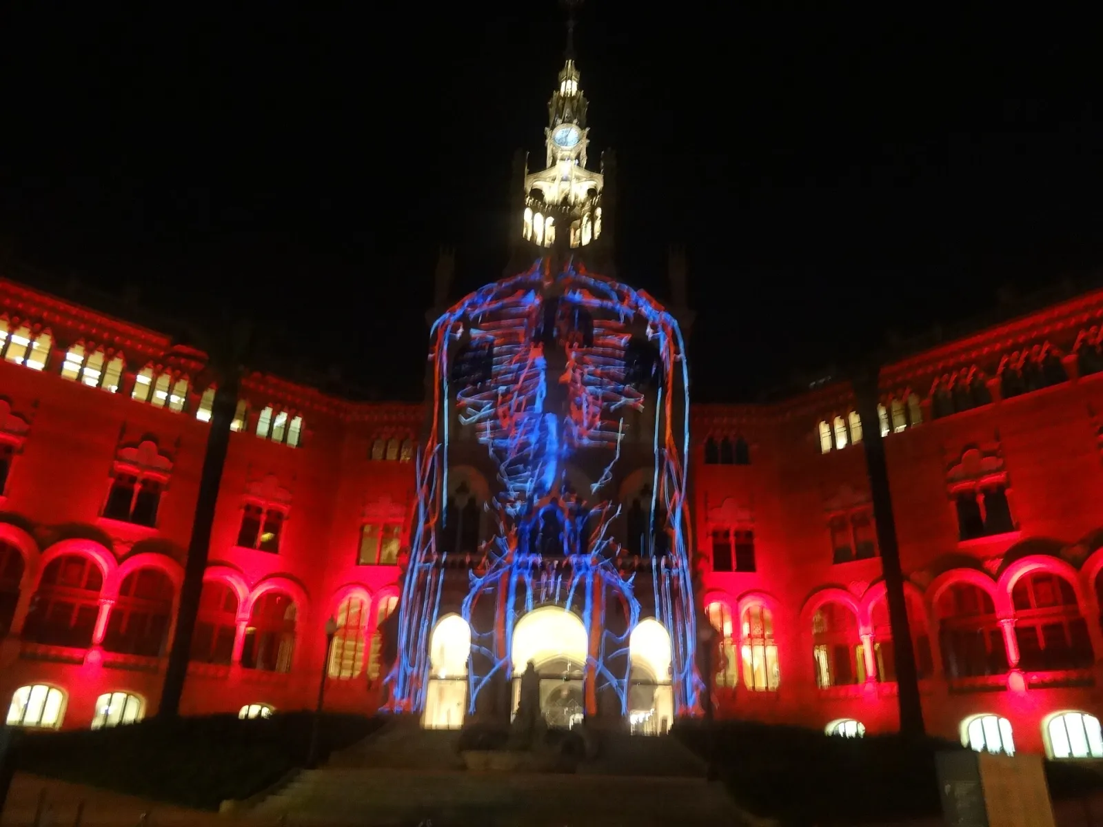 A modernist hospital building in Barcelona lit in red and gold by a projection mapping show on New Year's Day, windows and towers picked out.