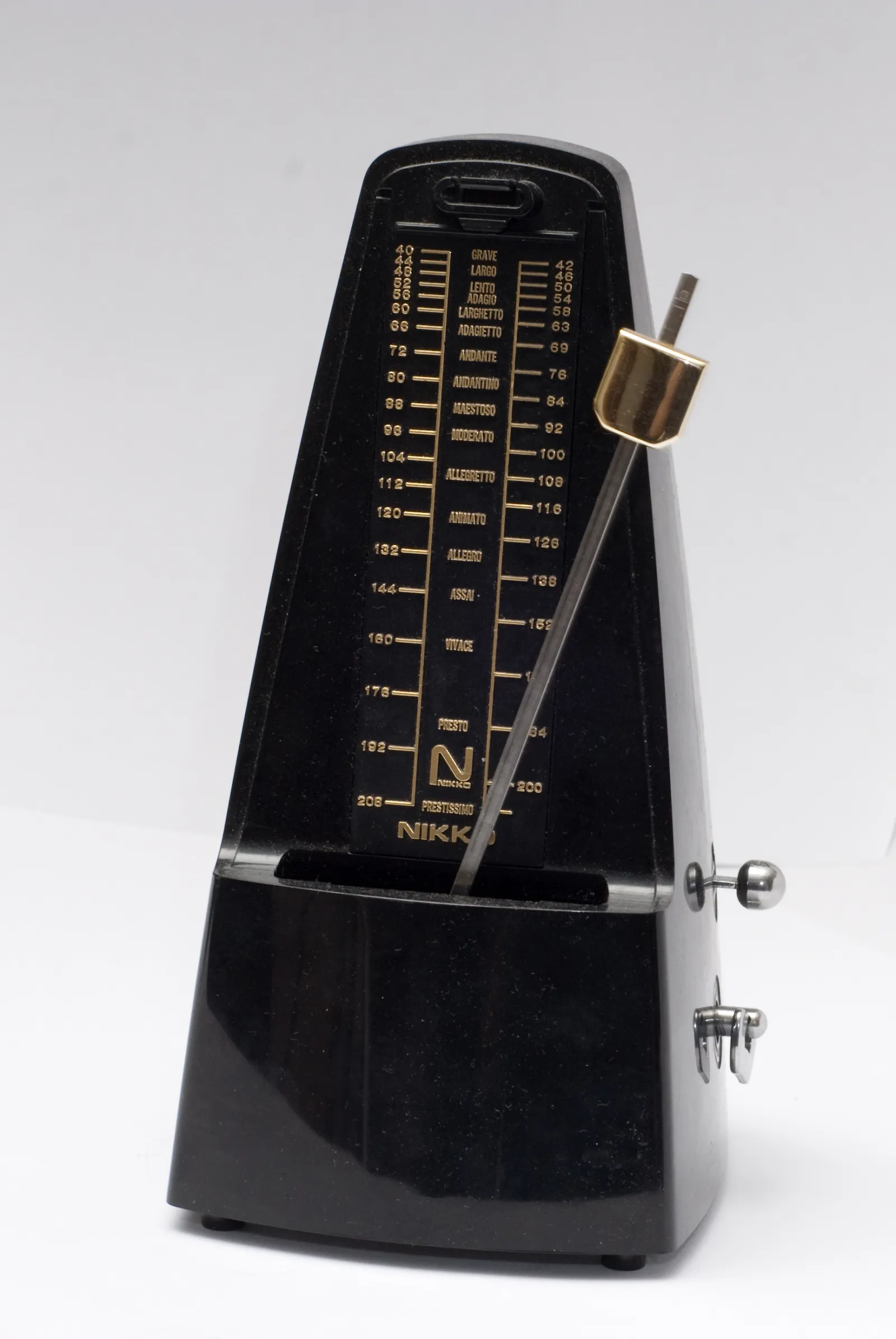 A black Nikko mechanical metronome with its pendulum swinging, the tempo scale printed behind it.