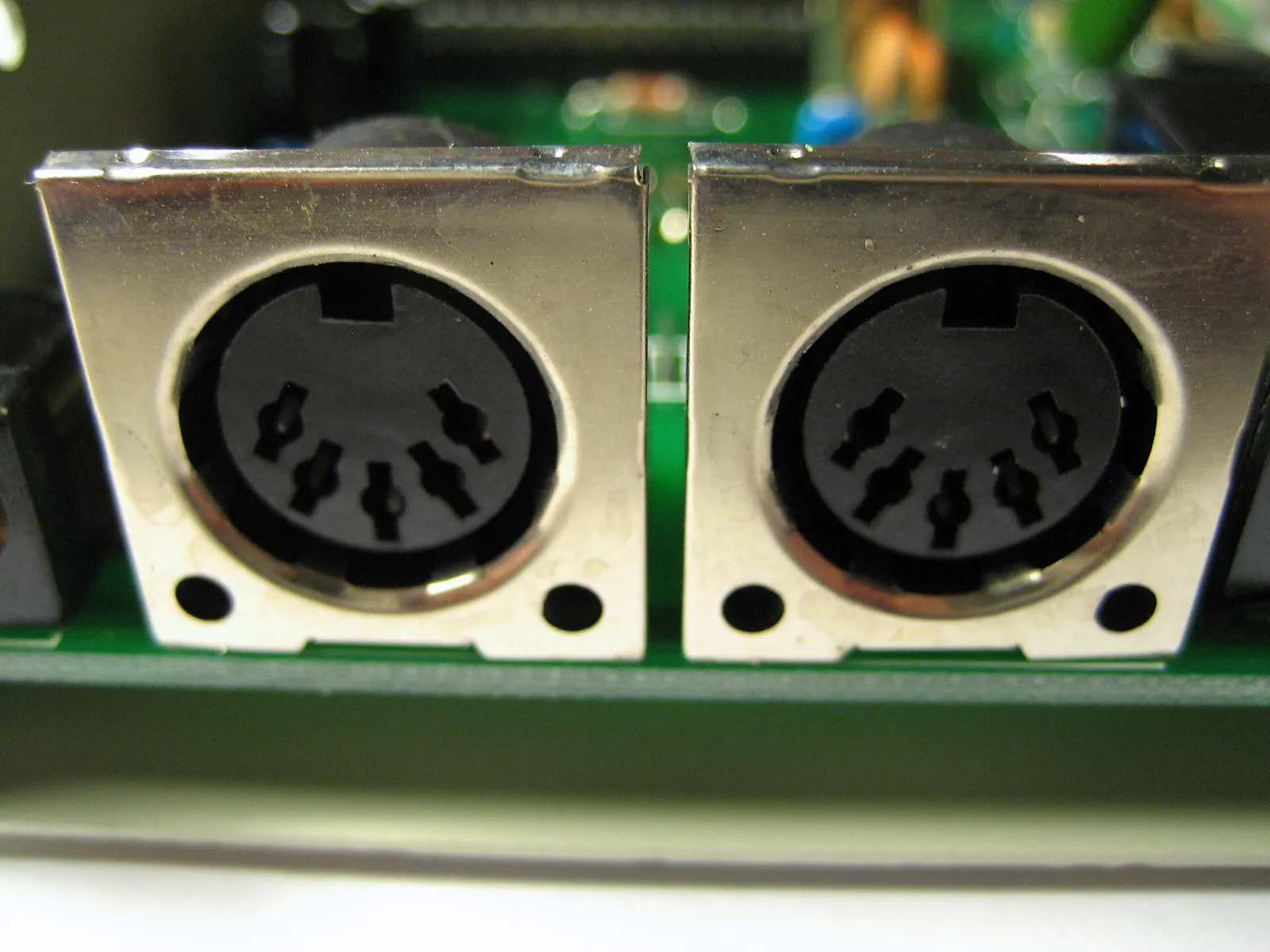 Close-up of two round five-pin MIDI DIN sockets on a green circuit board inside a metal case.