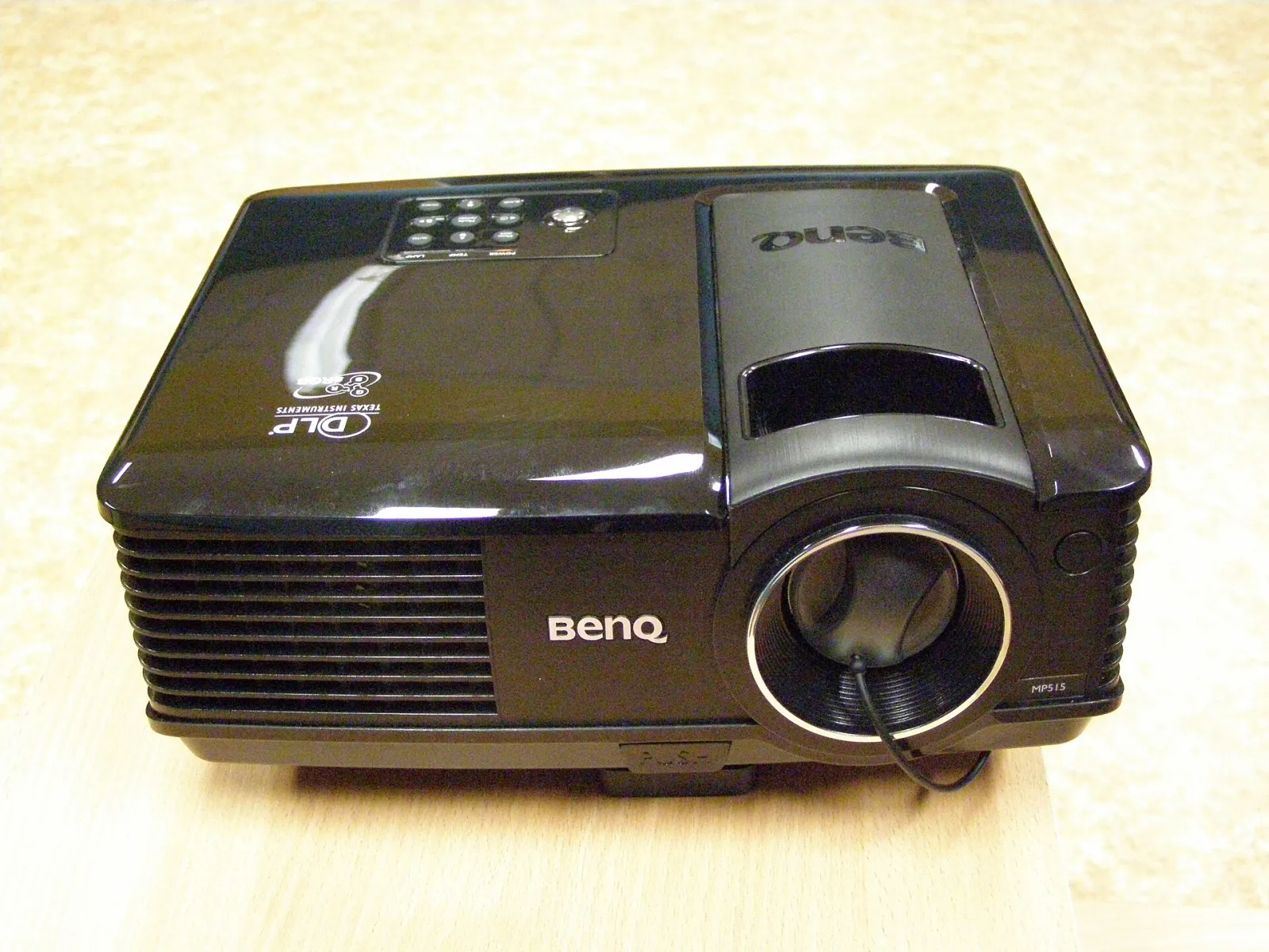 A compact black BenQ DLP projector on a table, lens at the front and controls on top.
