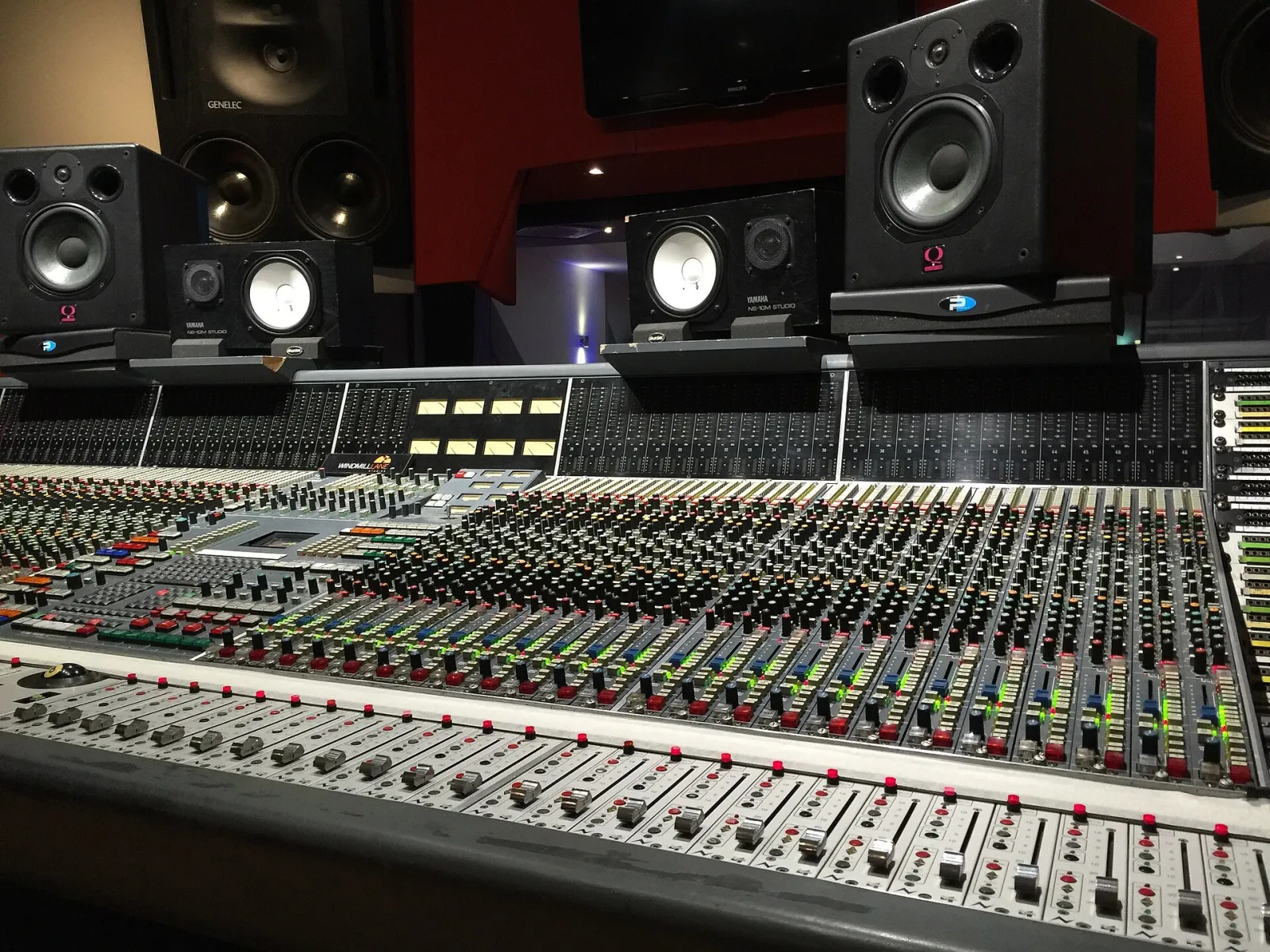 A large Neve mixing console in a recording studio control room, rows of faders and knobs, with studio monitors on the wall behind.