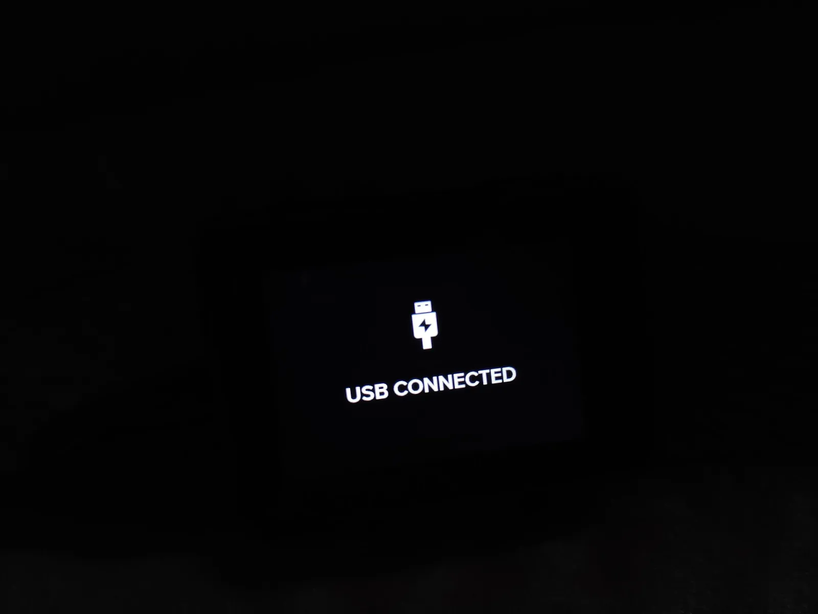 A small device screen in the dark showing a USB symbol and the words USB CONNECTED.